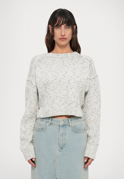 Gray, cropped sweater with a textured knit pattern and wide sleeves, paired with a light blue denim skirt featuring a front slit.