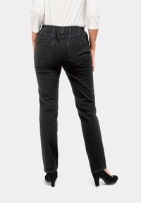 Pantalons en denim noir avec une taille élastique et des poches arrière. Les jambes sont droites et ils sont portés avec des chaussures à talons hauts noires.