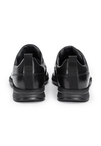Le scarpe in pelle nere presentano un colletto imbottito, un tassello posteriore testurizzato e una suola in gomma. La parte superiore è liscia con un design minimalista.