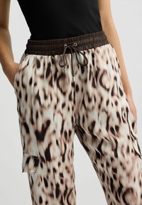 Jagtpants i leopardprint med en beige og brun farveskala, der har en elastisk talje med snøre og sidelommer.