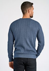 Blauer Kabelstrickpullover mit gerippten Bündchen und Saum, der ein strukturiertes Muster aufweist. Die Rückansicht zeigt einen runden Ausschnitt und eine figurbetonte Silhouette.