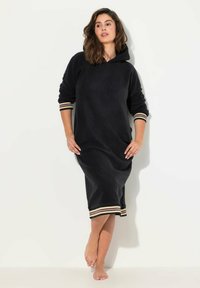Czarna dresowa sukienka z polarowego materiału o luźnym kroju, długimi rękawami i prążkowanymi mankietami w paski. Posiada kieszeń z przodu oraz długość do połowy łydki.