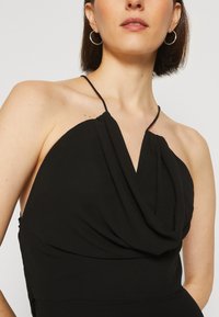 Rochie neagră fără mâneci, cu un decolteu drapat, bretele subțiri și o textură moale a țesăturii, având o siluetă ajustată și detalii de design minime.