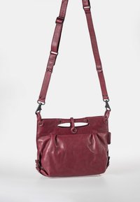 Burgunderfarbenes Leder-Crossbody-Tasche mit verstellbarem Tragegurt, vorderer Drapierung, runden Aussparungen und metallenen Akzenten. Glatte Textur.
