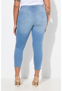 Jeans capri de mezclilla azul claro con un diseño ajustado, dos bolsillos traseros y un dobladillo que termina justo por encima del tobillo, combinados con tacones beige.