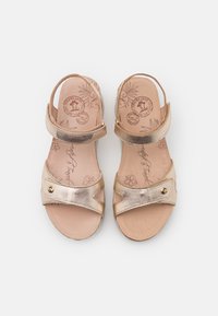 Μεταλλικά χρυσά σανδάλια με ρυθμιζόμενες ταινίες, υφή στο εσωτερικό, και διακοσμητικά κουμπιά. Εσωτερική επιφάνεια με λουλουδάτο σχέδιο. Ισιωτή σόλα.