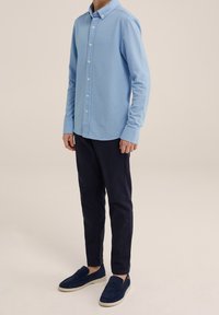 Světle modrá košile na knoflíky s dlouhými rukávy, spojená s tmavě modrými kalhotami a námořnickými slip-on botami. Jednoduchý design, bez viditelných vzorů.