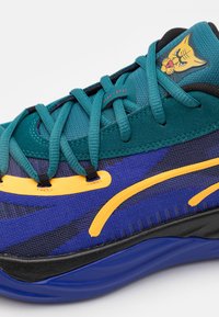 Sportschoen met een teal bovenkant, zwarte accenten en gele details. Beschikt over een textuurstof, een gemusterde zijkant en een kattenafbeelding op de tong.