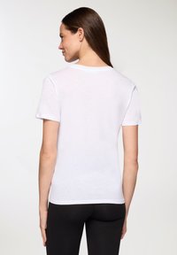 T-shirt bianca a maniche corte con collo rotondo, texture morbida, forma aderente e retro semplice, abbinata a leggings neri.
