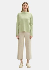 Hellgrüner Pullover mit hohem Kragen und langen Ärmeln, kombiniert mit cremefarbenen, weit geschnittenen Hosen und beigen Slippern.