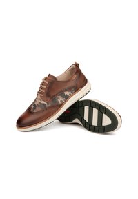 Chaussures en cuir marron avec un motif camouflage, bout rond et détails cousus. La semelle extérieure est blanche avec un profil de crampons verts pour une meilleure adhérence.