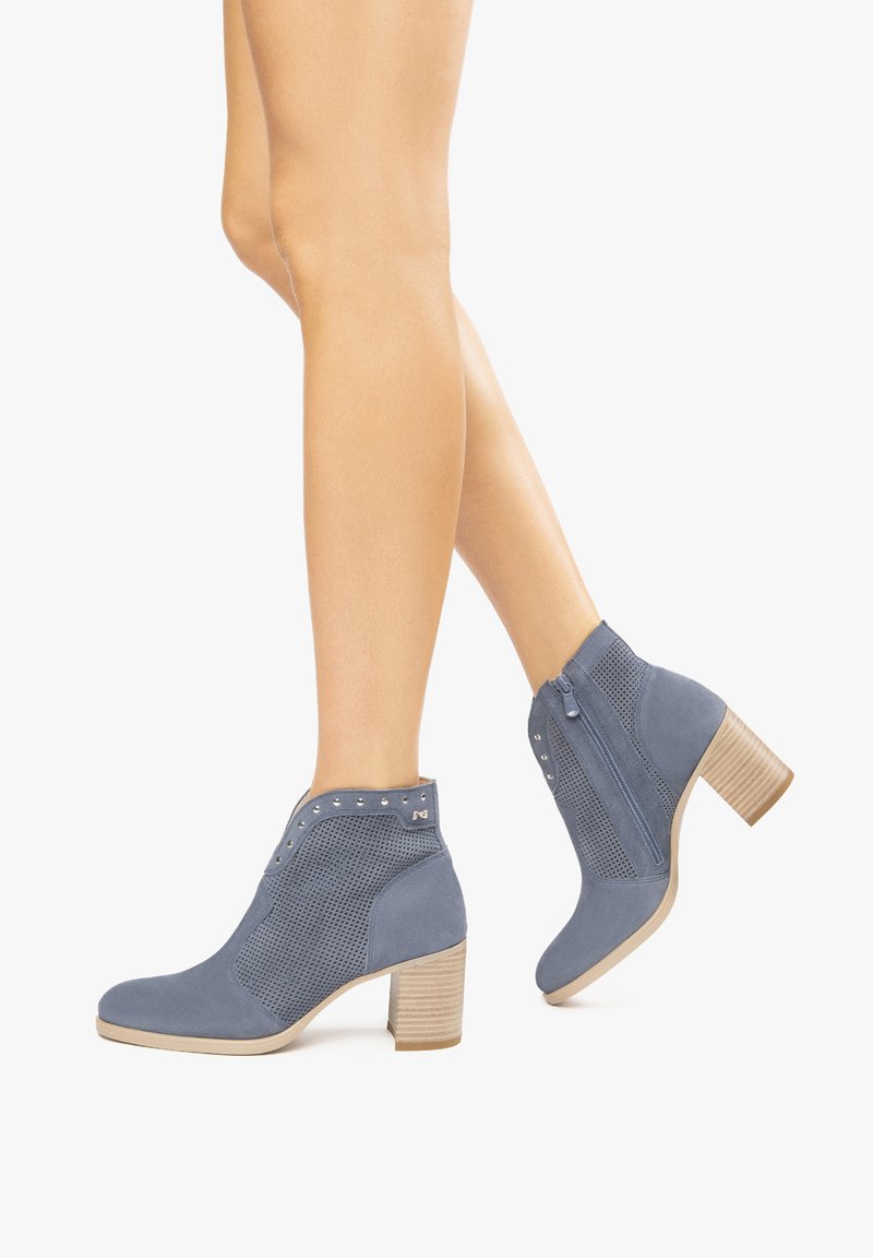 Bottines en daim bleu avec des panneaux perforés, une fermeture éclair sur le côté, un talon empilé et des clous décoratifs le long du bord supérieur.