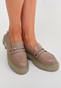 Loafer-stil Schuhe aus glattem taupefarbenem Leder mit einer dicken beigen Sohle, die ein dezentes Nahtdesign und dekorative Schnallenakzente aufweisen.