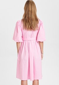 Rosa bomullsklänning med korta puffärmar, cinchad midja och en utsvängd kjol. Slät textur, midjelång design och enkla sömmar.