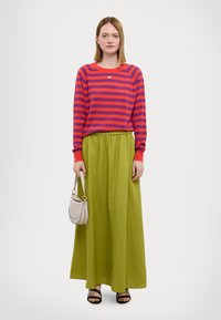 Maglione a maniche lunghe a strisce rosse e viola, abbinato a una gonna maxi verde con vita elasticizzata. Accessoriato con una piccola borsa beige.