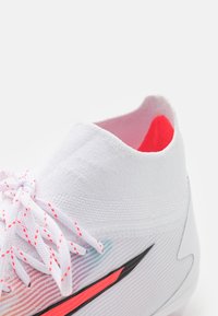 Scarpa sportiva bianca con collo alto, caratterizzata da un motivo gradiente e un accento nero e rosa vivace sul lato. Tomaia in tessuto testurizzato.
