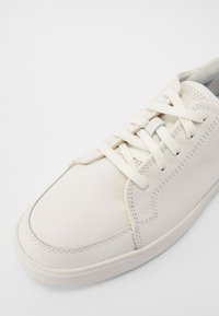 Tênis de couro branco com bico redondo, cadarços planos, costura discreta e sola de borracha. Textura suave e design minimalista sem padrões.