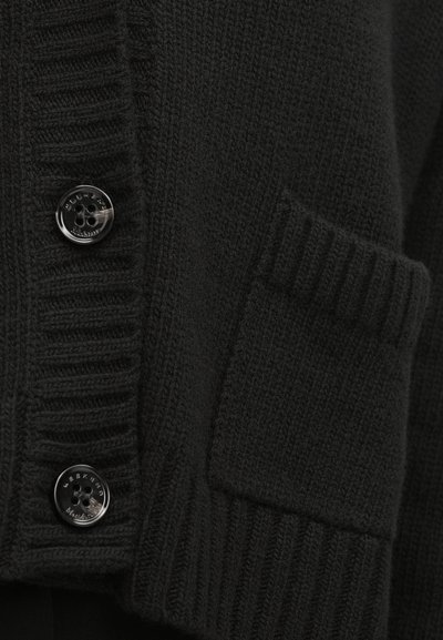 Μαύρη πλεκτή ζακέτα με ριμπ γιακά, δύο μεγάλα μαύρα κουμπιά και μια τσέπη με κεντημένη λεπτομέρεια στο μπροστινό μέρος.