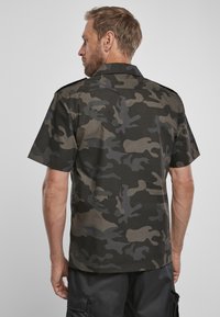 Camicetta a maniche corte in motivo mimetico nero e grigio. Presenta un colletto strutturato e spalline sulle spalle. Tessuto morbido al tatto.