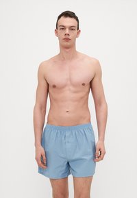 Shorts en coton bleu clair avec taille élastique et détail de bouton à l'avant, présentant une texture lisse et une coupe décontractée.