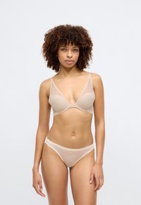 Μπεζ σετ εσωρούχων που περιλαμβάνει ένα διάφανο σουτιέν με λεπτομέρειες από δίχτυ και αντίστοιχο στρινγκ. Απλός σχεδιασμός, λεία υφή με διακριτική σήμανση.