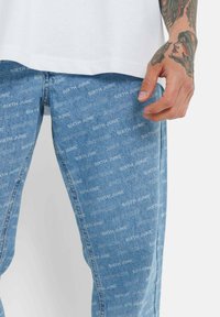 Jeans de mezclilla azul claro con un estampado repetido de "SIXTH JUNE" en todo el tejido. Diseño de pierna recta con un estilo clásico de cinco bolsillos.