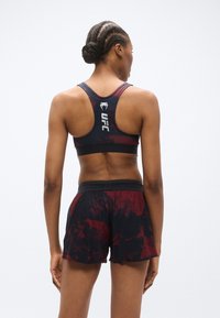 Brassière de sport noire et rouge à motif avec un dos nageur et un logo ; associée à un short de sport assorti noir et rouge avec une taille élastique.