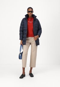 Navy puffer jacket, red sweater, beige chinos, black slip-ons. Blue handbag features a strap. Sunglasses complete the outfit.