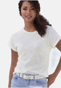 Weißes strukturiertes Kurzarm-T-Shirt mit aufgerollten Ärmeln, kombiniert mit hellblauen Jeans und einem weißen perforierten Gürtel.