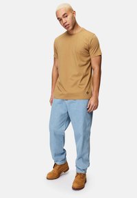 Tan crew-neck kortærmet t-shirt, afslappet pasform, parret med lyseblå baggy jeans og brune snørebåndsstøvler. Minimalistisk logo detaljer på skjorten.