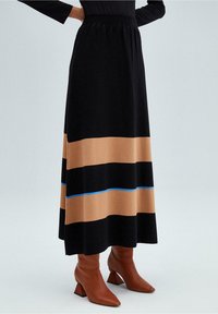 Falda larga negra con rayas horizontales marrones y azules, hecha de tela suave, combinada con botas marrones de tacón hasta el tobillo. Fondo liso.