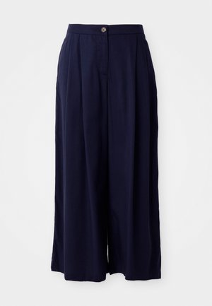 Temno modri široki hlače z visokim pasom, zapiranjem spredaj na gumb in nagubanimi detajli na beli podlagi.