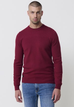 Suéter de punto burdeos con un patrón texturizado, cuello redondo y puños acanalados. Combinado con jeans azules, que presentan un diseño de corte slim.