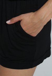 Zwarte stoffen shorts hebben een zijzak. Het materiaal is smooth met een lichte glans; de tailleband is geraapt voor comfort.