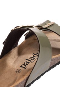 Sandalias verdes de charol con plantilla de corcho marrón, que presentan correas dobles y un detalle de hebilla en tono dorado. Logo impreso en la plantilla.