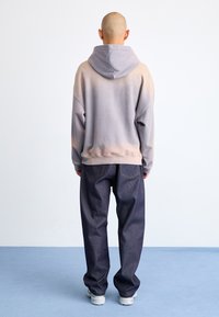 Light purple to beige gradient oversized hoodie with a drawstring and ribbed cuffs, paired with dark blue baggy jeans.