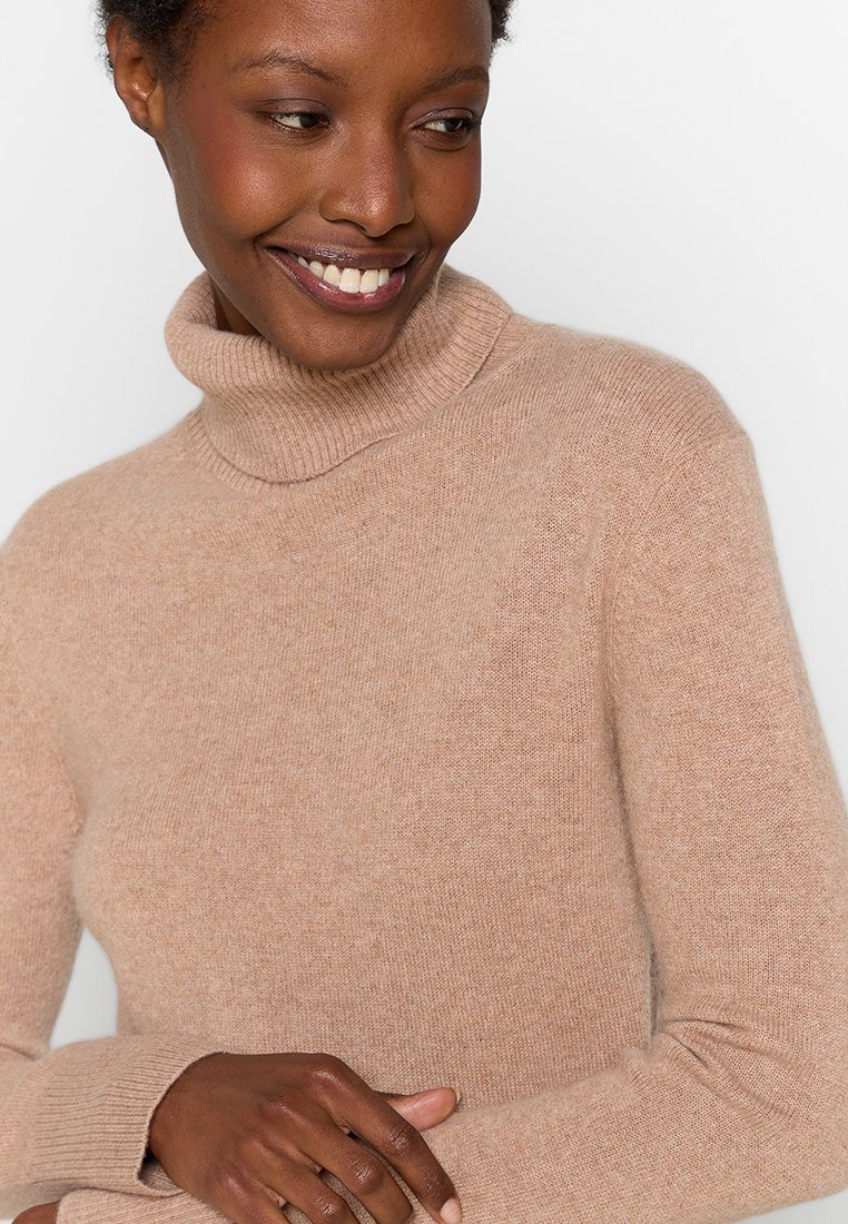 Beżowy sweter z golfem, wykonany z miękkiego, teksturowanego materiału, charakteryzujący się dopasowanym krojem oraz prążkowanym kołnierzem. Subtelne szwy podkreślają ogólny wygląd.