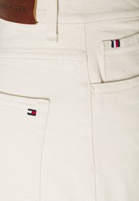 Jeans de mezclilla blanca con un parche de cuero marrón de la marca y un pequeño acento bordado multicolor en el bolsillo trasero.