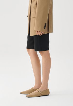 Kollane nubukist libised kingad terava nina ja väikese pandla aktsendiga. Kandsid mustade lühikeste pükste ja beeži ülekäitmise bleiseriga.