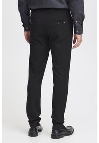 Czarne spodnie o slim fit, z tylną kieszenią, subtelnymi detalami szycia i teksturowanym materiałem. Noszone z czarnymi butami.
