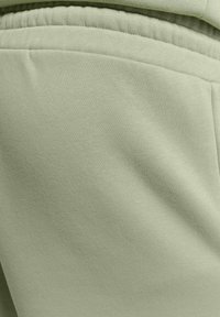 Lichtgroene stof met een gladde textuur en een elastische tailleband. Zichtbare stiksels brengen extra nadruk aan het ontwerp van het materiaal.