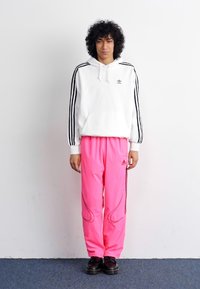 White hooded sweatshirt with black stripes, paired with vibrant pink track pants featuring black accents, and black shoes.