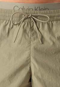 Bežové kraťasy Calvin Klein s textúrovanou látkou, elastickým pásom so vzorom a sťahovacou šnúrkou s kovovými koncami.