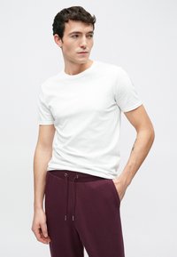 Λευκό κοντομάνικο μπλουζάκι με απλό σχέδιο, συνδυασμένο με μπορντό φόρμα με κορδόνι στη μέση, πλευρικές τσέπες και λεία υφή.