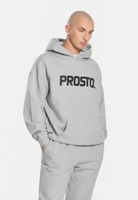 Szara bluza z kapturem wykonana z miękkiego materiału, z dużym czarnym logo "PROSTO." na przodzie, z kapturem na sznurku i kieszenią kangurkową.