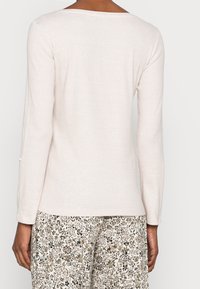 Helle beige langärmlige Bluse, gerippte Textur, Rundhalsausschnitt, mit Knopfdetails an den Ärmeln, kombiniert mit floral gemusterten Hosen.