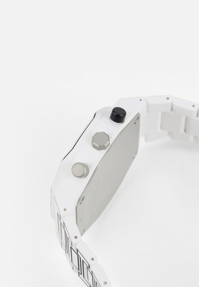 Hvidt ur med et geometrisk design, der har et plastrem. Urkassen har tre knapper: en sort, en sølvfarvet og en hexagonal.