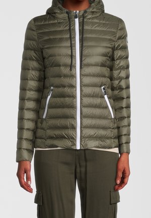 Personne portant une veste matelassée à capuche vert olive avec une fermeture éclair blanche et des poches zippées, assortie à un pantalon cargo.