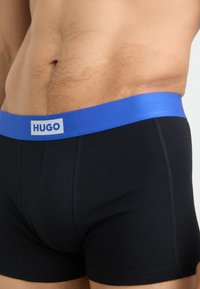 Black boxer briefs featuring a blue elastic waistband with the "HUGO" logo. The fabric appears smooth with a fitted design.