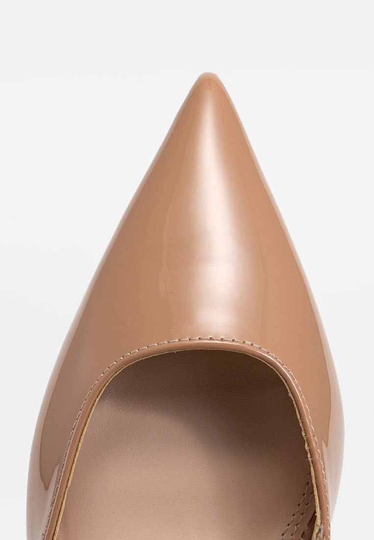 Naga, lakierowana szpilka w kolorze nude z wysmukłą końcówką i otwartymi bokami, charakteryzująca się gładką, błyszczącą powierzchnią i minimalnymi szwami.